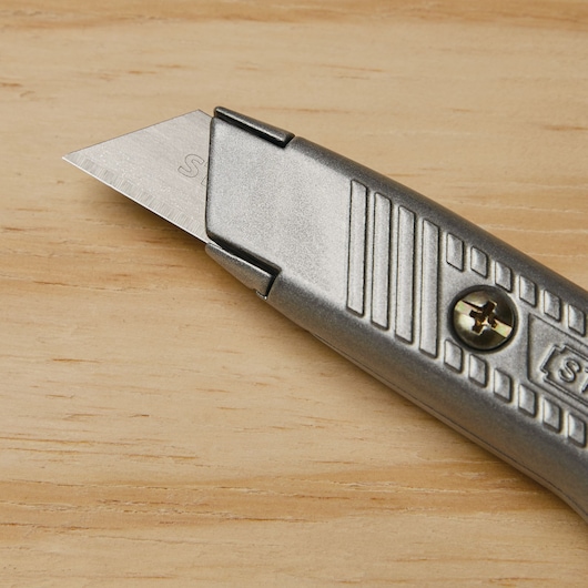 STANLEY 10-299 utility knife with silver metal body and exposed blade, angled close-up on wood surface.