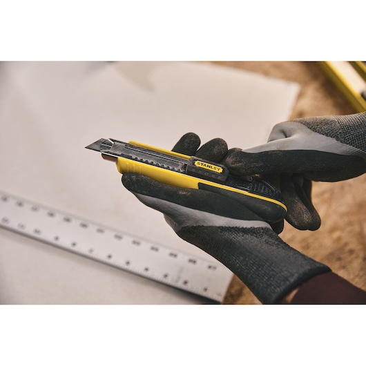 Photo of STANLEY 10-481 utility knife held in gloved hands, yellow and black, near a metal ruler.