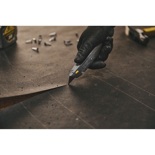 Photo of STANLEY 10-499 utility knife cutting material on work surface, hand in black glove holds knife.