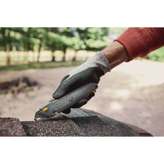 Photo of STANLEY 10-499 utility knife being used by a gloved hand to cut roofing material outdoors.