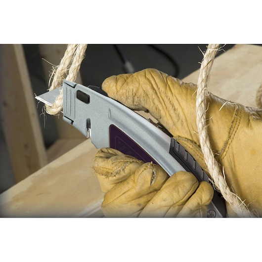 Photo of gloved hand using STANLEY 10-788 utility knife to cut thick rope on wood surface.