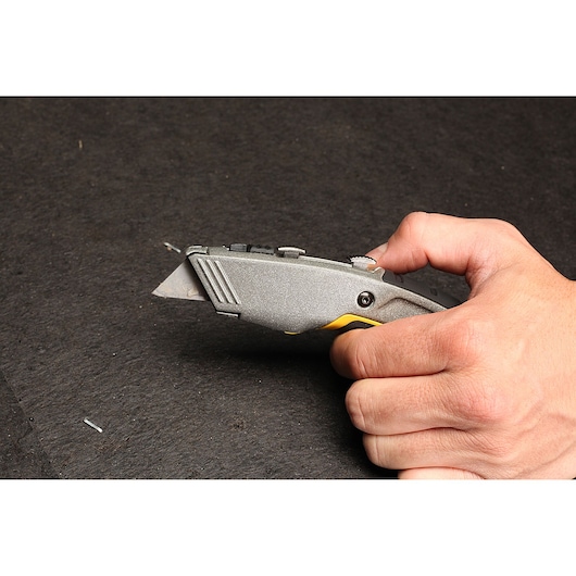Photo of STANLEY 10-789 utility knife in hand, silver with yellow accents, cutting material.