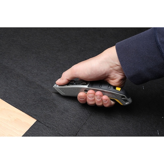 STANLEY 10-789 utility knife cutting black material, shown in hand in use.