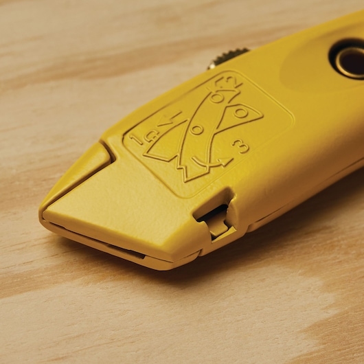 Stanley 10-989 yellow utility knife close-up on wood surface, showing engraved blade change diagram.