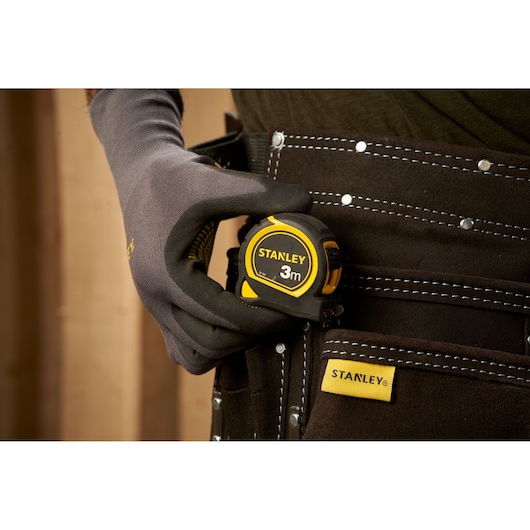 STANLEY 30-787 tape measure, 3m, held by a gloved hand and clipped to a tool belt, close-up photography.