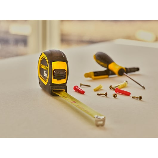 STANLEY 30-797 tape measure and screwdriver with screws and wall plugs on tabletop, angled view.