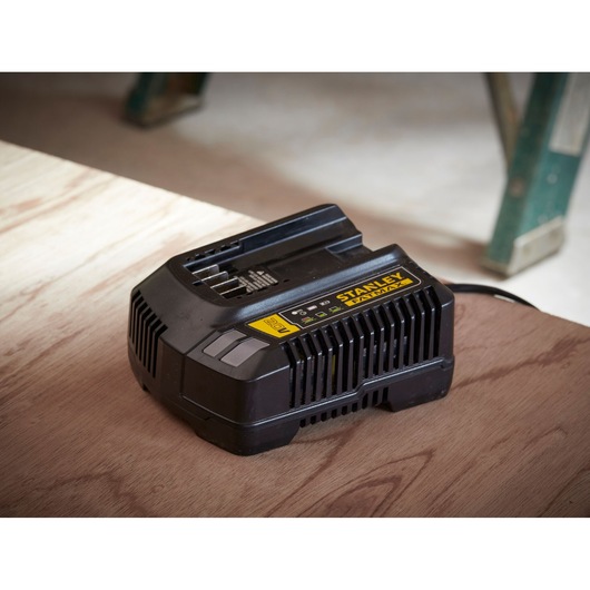 Stanley SC200 battery charger, black with yellow label, angled on wooden surface in workshop.