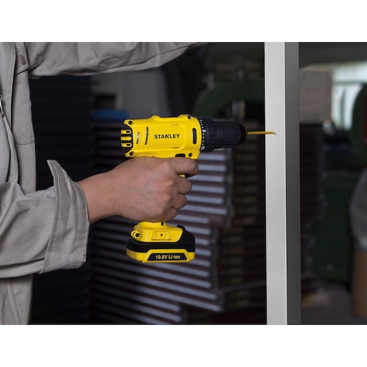 STANLEY SCD12S2K cordless drill being used to drill into metal, yellow and black with 10.8V Li-Ion battery.