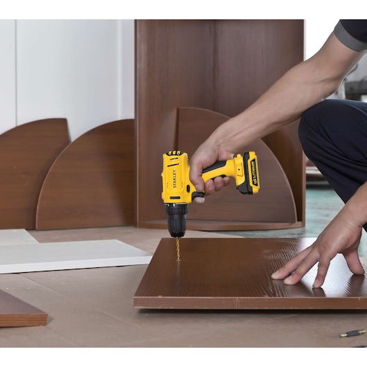 STANLEY SCD12S2K cordless drill in use on brown wood panel, close-up, product photography.