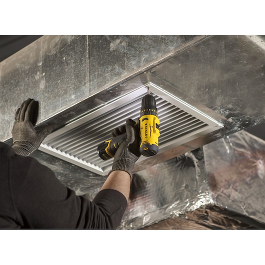 Photo of STANLEY SCH10 cordless drill used to install HVAC vent, close-up of worker's hands.