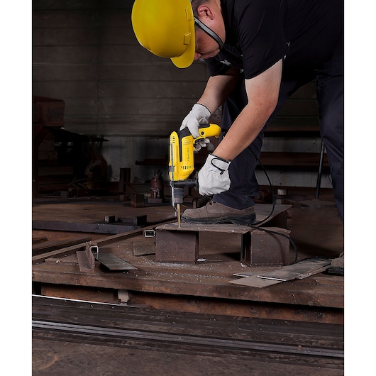 Worker uses STANLEY SDH700 corded drill on metal, wearing gloves and hard hat, industrial setting.