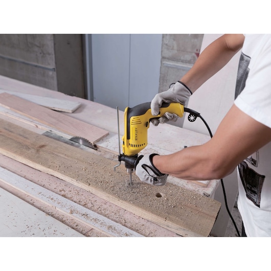 Photo of a person using a STANLEY SDH700 electric drill on wood in a workshop.