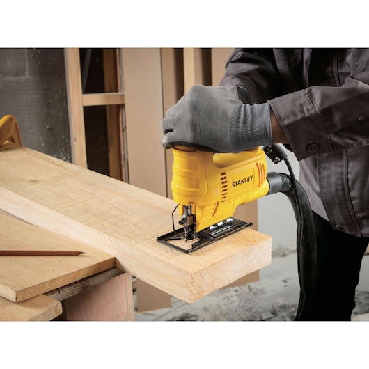 STANLEY SJ45 jigsaw cutting wood, yellow tool in use by a gloved hand at workbench.