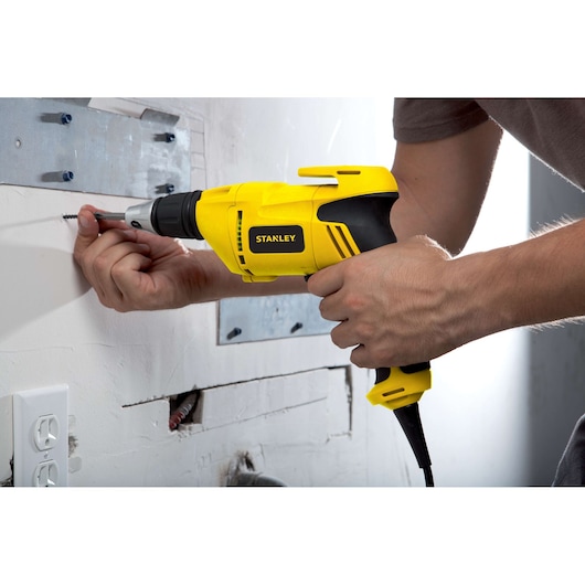 STANLEY STDR5206 corded screwdriver, yellow and black, used on wall during installation.