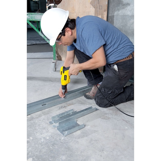 STANLEY STDR5206 corded drill in use on metal studs by worker wearing hard hat, side angle, photography.