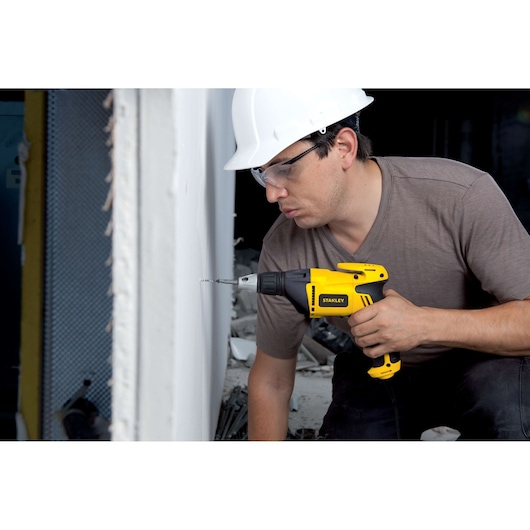 STANLEY STDR5206 yellow corded drill in use by a worker drilling into a wall on a construction site.