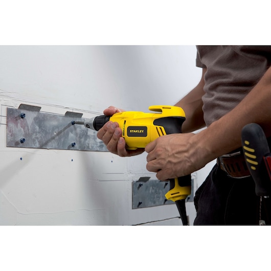 Stanley STDR5206 yellow power drill used to attach metal plate to wall, close-up side angle.