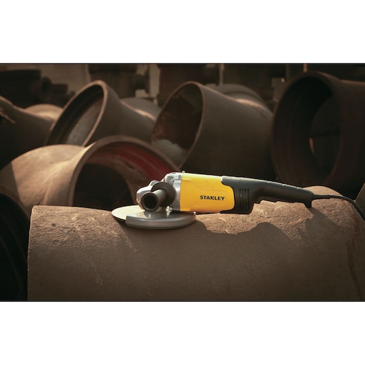 STANLEY STGL2223 angle grinder with yellow and black body placed on metal pipes, side view.