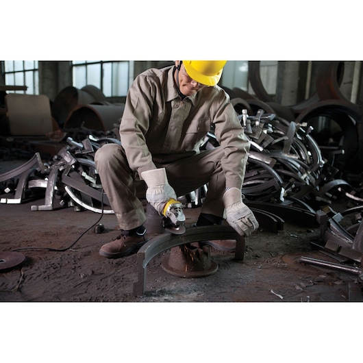STANLEY STGS8115 angle grinder in use by worker wearing protective gear, grinding metal in industrial setting.