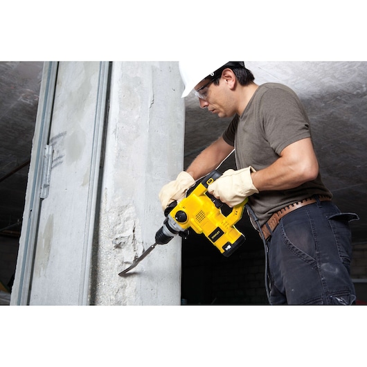 Photo of worker using STANLEY STHR1232K yellow rotary hammer drill on concrete wall, product in use.