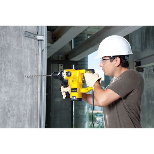 STANLEY STHR1232K rotary hammer drill in use, drilling concrete wall at construction site.