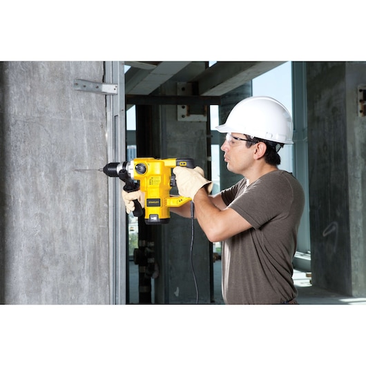 Stanley STHR1232K rotary hammer drill used by worker in gloves and helmet drilling concrete wall.