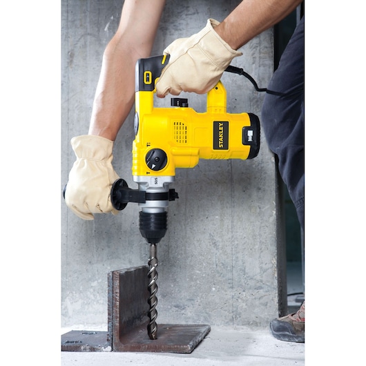 STANLEY STHR1232K rotary hammer drill being used to drill through metal, shown from side angle.