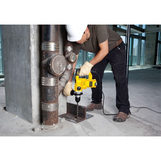 STANLEY STHR1232K hammer drill used by worker with gloves and helmet drilling metal in construction site.