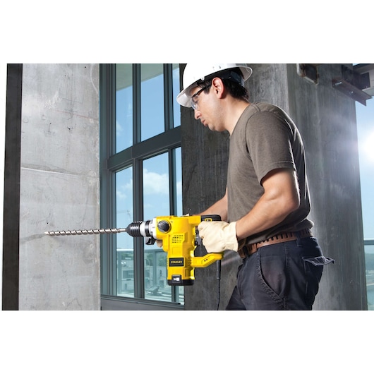 STANLEY STHR1232K rotary hammer drill in use, drilling into concrete wall at construction site.