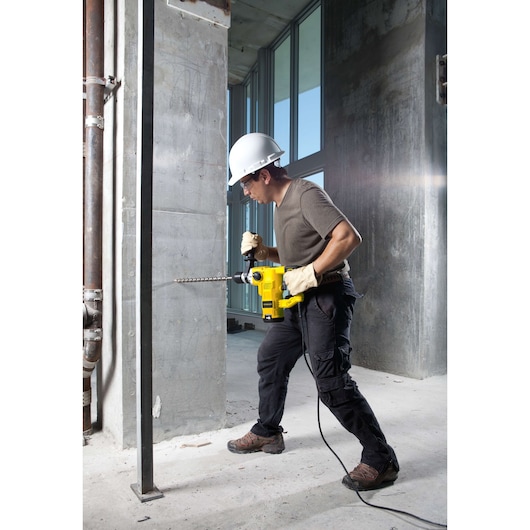 STANLEY STHR1232K rotary hammer in use drilling into concrete wall at a construction site, side view.