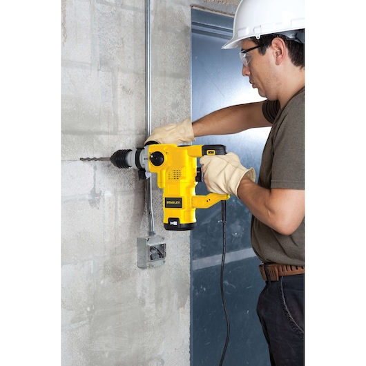 STANLEY STHR1232K rotary hammer drill in use drilling into concrete wall, side view, worker wearing safety gear.