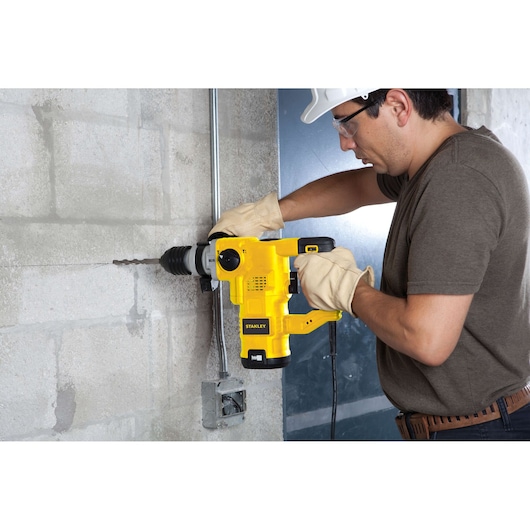 STANLEY STHR1232K rotary hammer drill in use on concrete wall, side view, yellow tool with gloves.