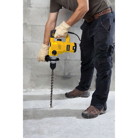 STANLEY STHR1232K rotary hammer drill in use on concrete floor, shown from side angle.