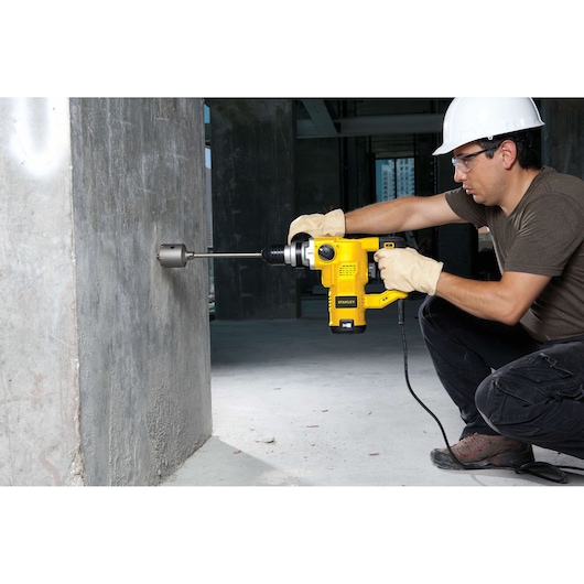 Photo of STANLEY STHR1232K rotary hammer in use drilling into a concrete wall at a construction site.