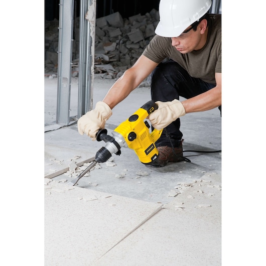 Photo of STANLEY STHR1232K rotary hammer in use, breaking floor tiles at a construction site.