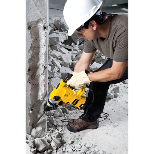 Photo of worker using STANLEY STHR1232K demolition hammer on concrete wall at construction site.