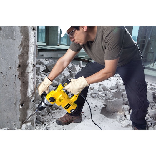 STANLEY STHR1232K rotary hammer drill in use on concrete wall, construction setting, side angle.