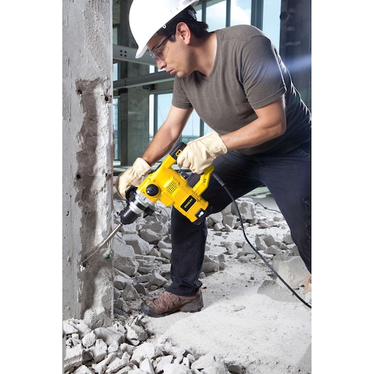 STANLEY STHR1232K rotary hammer drill in use breaking concrete, worker wearing gloves and hard hat.