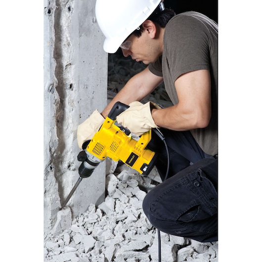 Worker using STANLEY STHR1232K demolition hammer to break concrete, wearing gloves and hard hat.
