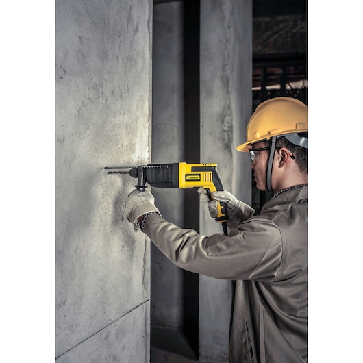 Stanley STHR202K rotary hammer drill used on concrete wall, construction setting, yellow and black tool.