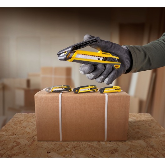 Photo of STANLEY STHT10501 utility knives in yellow and black, one held by a gloved hand, others on a cardboard box.