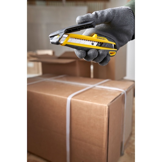 Photo of STANLEY STHT10501 utility knife held by gloved hand over cardboard boxes, side view.