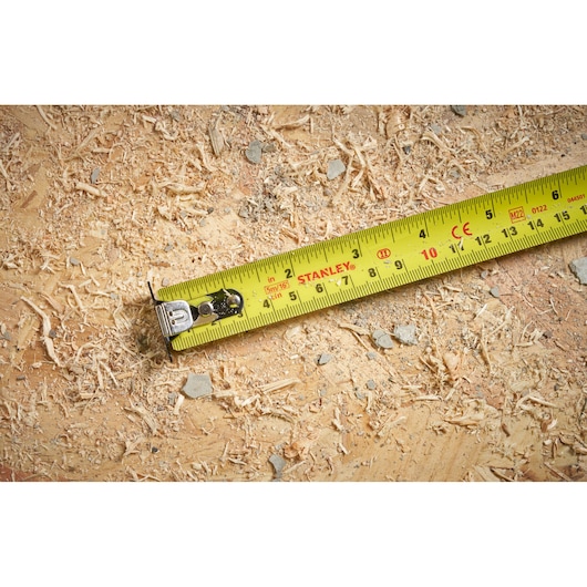 Stanley STHT37235-5 yellow tape measure on wood surface with sawdust and debris.