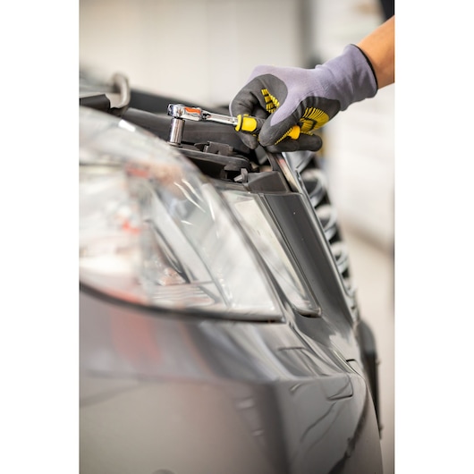 STANLEY STMT82828-LA ratchet tool in use on car headlight, close-up angle, gloved hand holding.