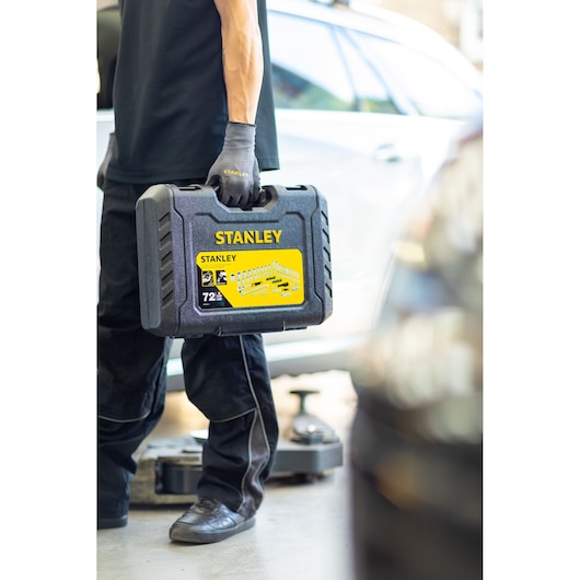 Photo of person holding STANLEY STMT82828-LA black hard plastic tool case, outdoors near a car, product label visible.