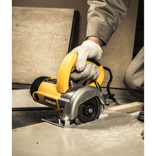 Photo of STANLEY STSP125K tile cutter saw in use on ceramic tile, close-up side angle, yellow and silver finish.