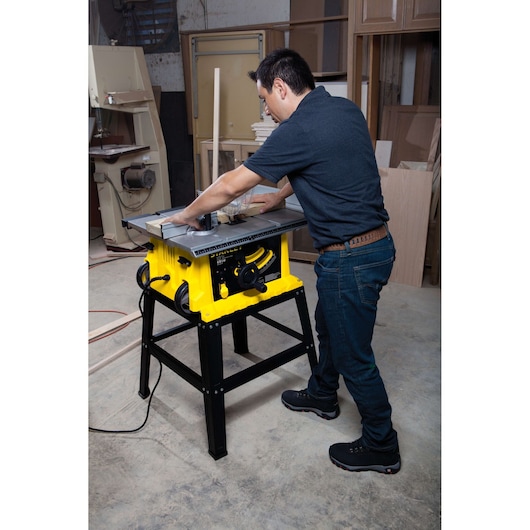 STANLEY STST1825 table saw in use in a workshop, man cutting wood on yellow and black saw.