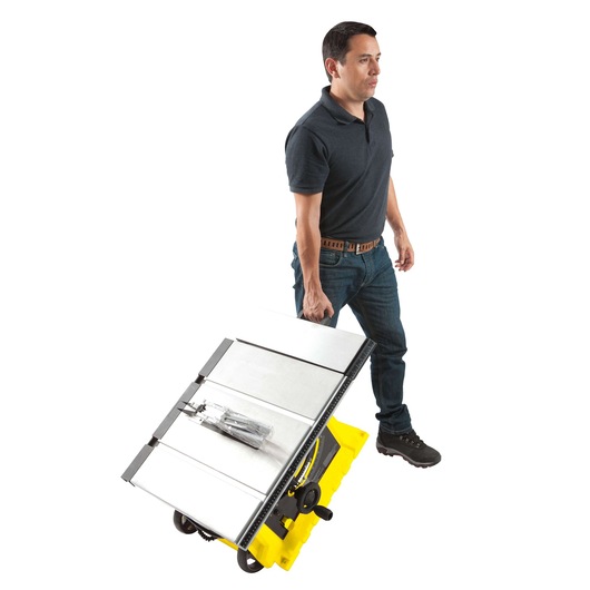Photo of a man carrying a STANLEY STST1825 portable table saw with yellow base, side angle view.