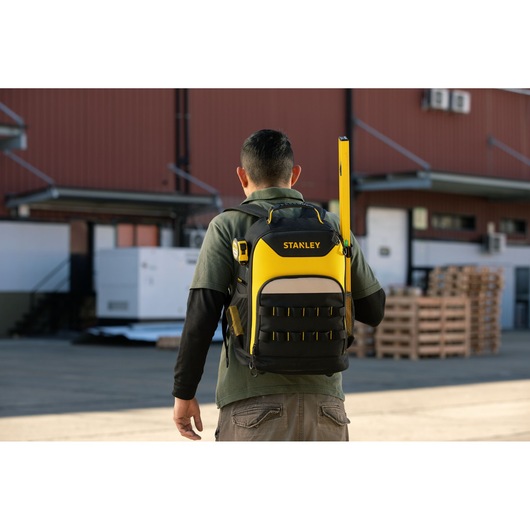 Photo of STANLEY backpack, SKU STST515155LA, black and yellow, worn outdoors with tools inserted in pockets.