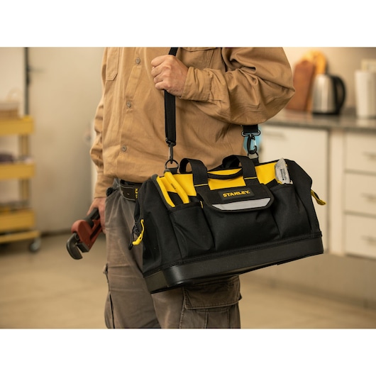 Photo of STANLEY tool bag STST516126LA with yellow handles, carried by a person in a workshop.